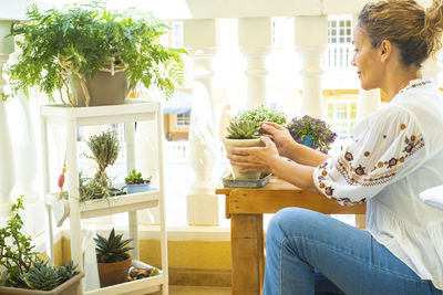 Young woman holding potted plant sitting in balcony