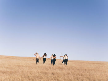 Rear view of men and women running on field against clear sky