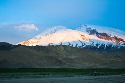 Person riding moped on dirt road against muztagh ata