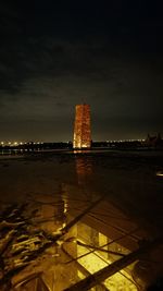 Illuminated city by sea against sky at night