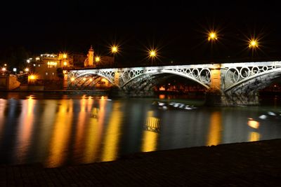 Illuminated bridge over river against sky in city at night