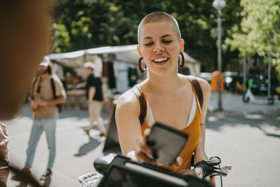 Smiling woman with shaved head paying via tap to pay while shopping at flea market