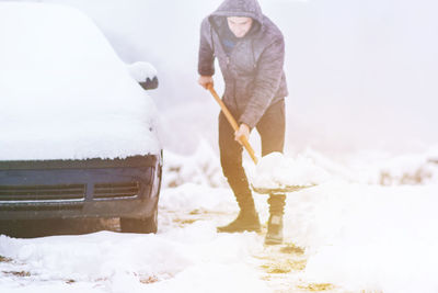 Full length of man shoveling snow by car outdoors