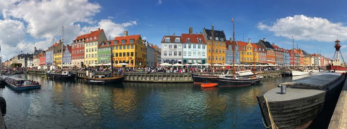 Sailboats moored on river by buildings in city against sky