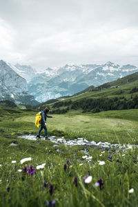 Side view of woman walking by flowering plants against mountains and sky