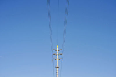 Low angle view of electricity pylon against clear blue sky