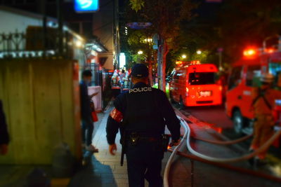 Rear view of man walking on illuminated street at night