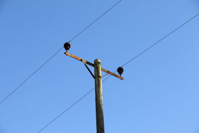 Low angle view of telephone pole against clear blue sky