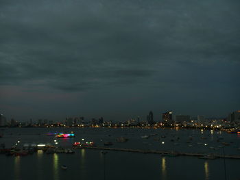 Illuminated city by sea against sky at night