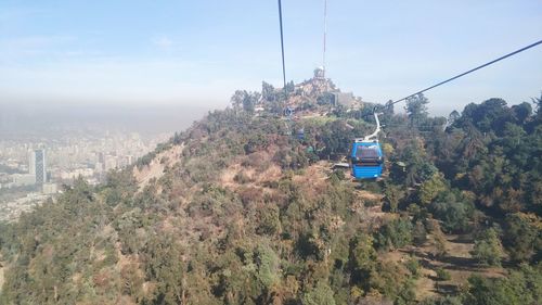Overhead cable car amidst trees and buildings against sky