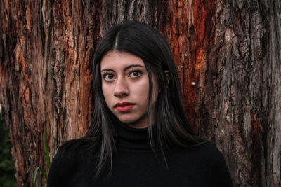 Portrait of young woman leaning against tree