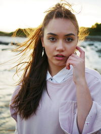 Close-up portrait of young woman with tousled hair standing against sea