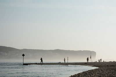 Silhouette people on beach against sky