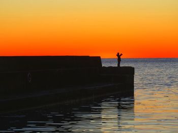 Silhouette man standing by sea against orange sky
