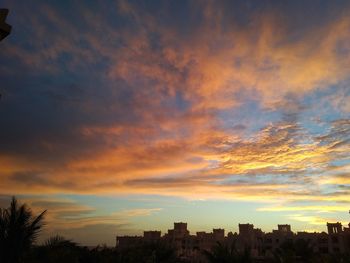 Silhouette of city against cloudy sky during sunset