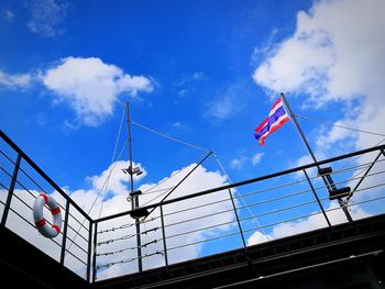 Low angle view of flag and life belt on railing of ship against sky