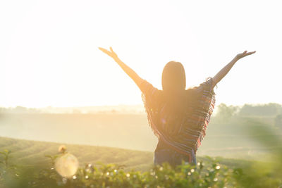 Rear view of woman with arms raised on field against sky