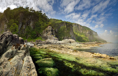 Scenic view of rocky mountains by sea against sky