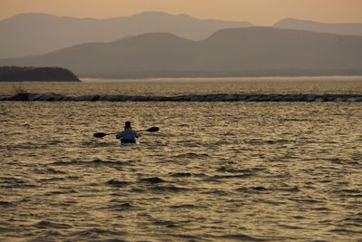 Man rowing boat in lake during sunset