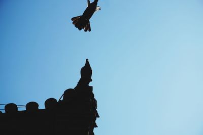 Low angle view of silhouette birds flying against clear blue sky