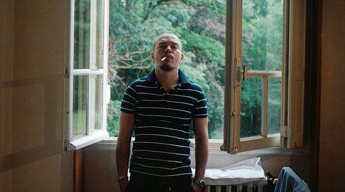 Portrait of young man smoking while standing by window at home