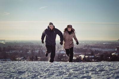 Full length of happy couple running on snow covered mountains