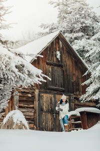 Smiling young woman standing on snow field against cottage