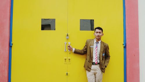 Portrait of smiling young man standing against yellow door