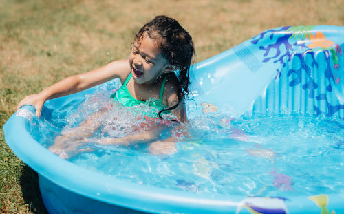 Mixed race young girl at home having fun on hot summer day in kiddie pool