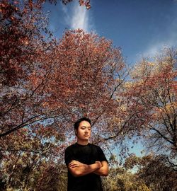 Portrait of young man standing by tree against cloudy sky during autumn.