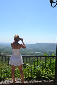 Rear view of young woman photographing mountains against clear sky