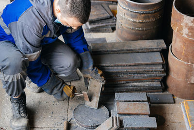 Worker in heavy industry or metallurgy beats scale off iron plates with hammer. work with metal