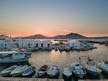 Boats moored in harbor at sunset