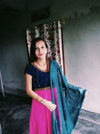 Portrait of beautiful young woman standing against wall