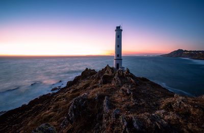 Lighthouse by sea against sky during sunset