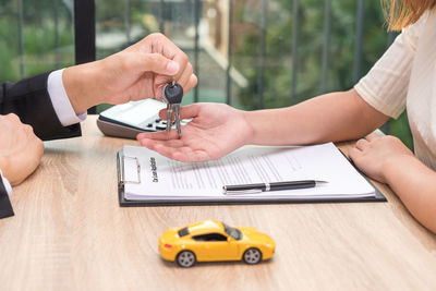 Cropped hand of businessman giving car keys to customer at desk in office