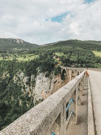 Woman standing by railing against cloudy sky