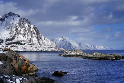 Scenic view of sea by snowcapped mountain against sky