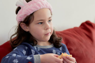 Cute little girl in a pink head dress is eating crepes on the couch