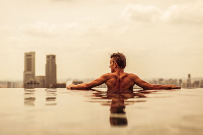 Rear view of shirtless man in swimming pool against sky