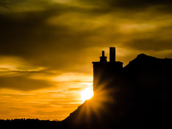 Silhouette hand by building against orange sky