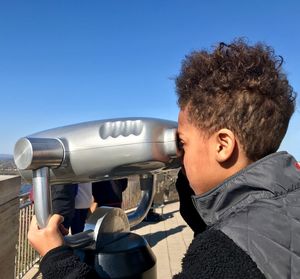 Portrait of boy holding camera against clear blue sky