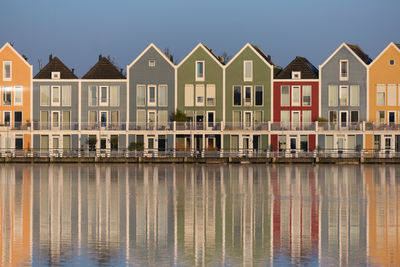 Colourful  lakeside houses reflected in houten against a clear blue sky.