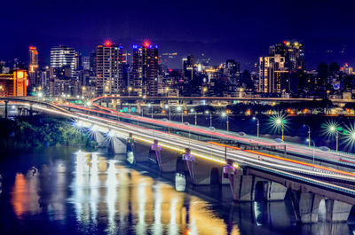 Light trails on bridge over river in city at night