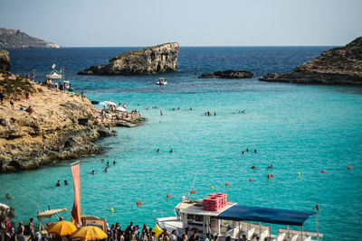 People on cliff by sea against clear blue sky