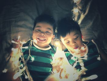 Portrait of boy with brother holding illuminated lights on bed