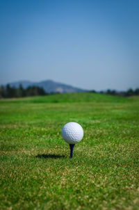 Golf ball with tee on grass against sky