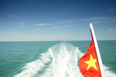 Vietnamese flag in sea against sky on sunny day