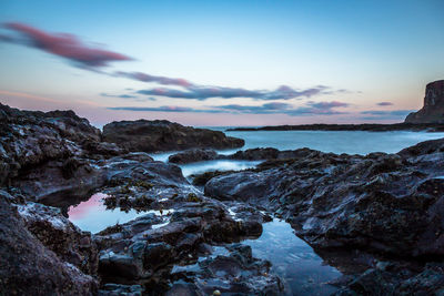 Rocks on beach against sky during sunset