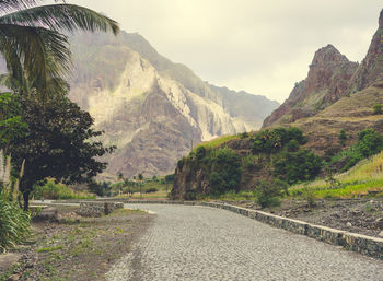 Road amidst trees and mountains against sky